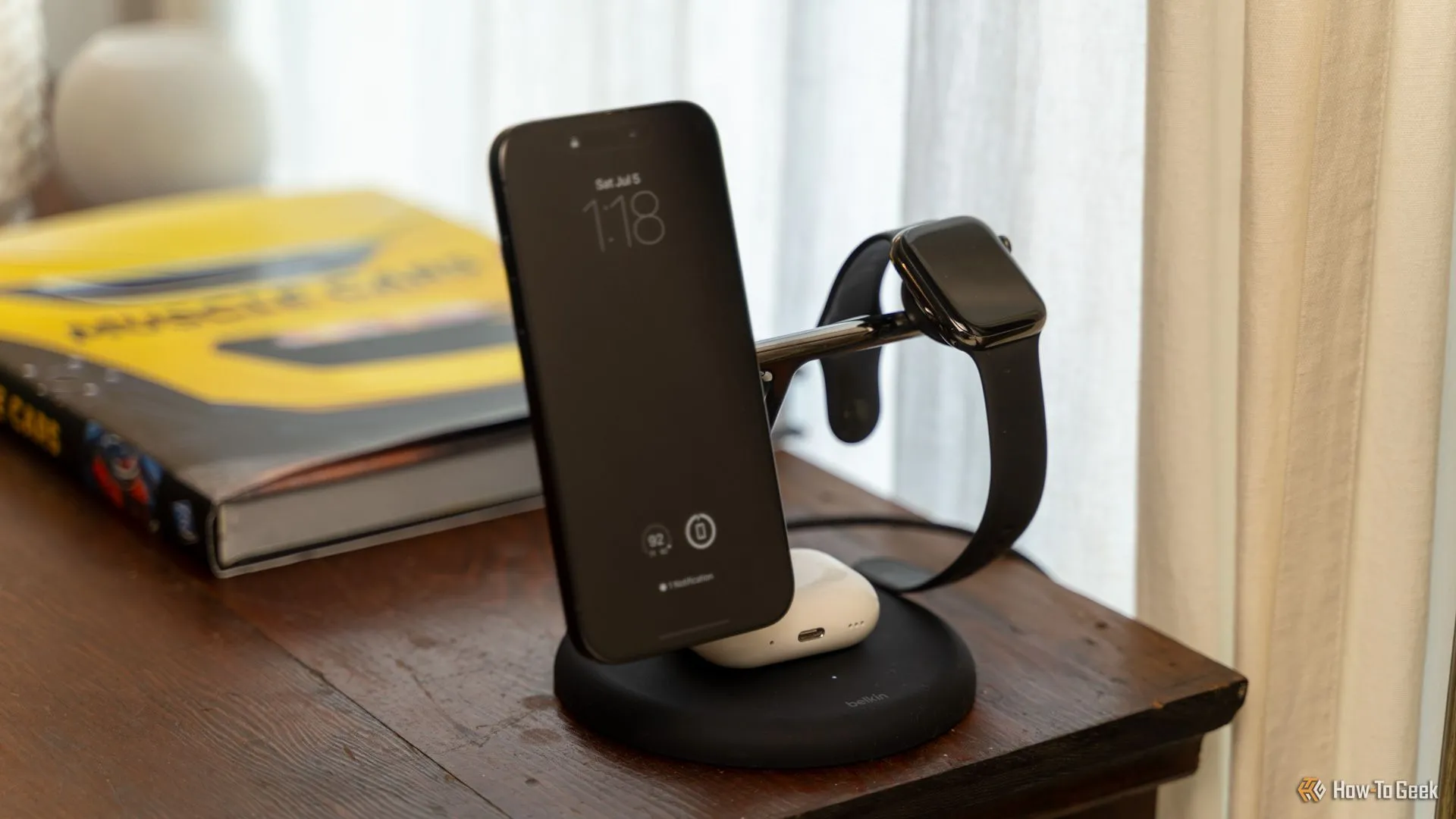 Bộ sạc Belkin BoostCharge Pro 3-in-1 MagSafe đang sạc cùng lúc iPhone, Apple Watch và AirPods, đặt gọn gàng trên bàn gỗ cạnh giường, thể hiện sự tiện lợi và tối ưu không gian.