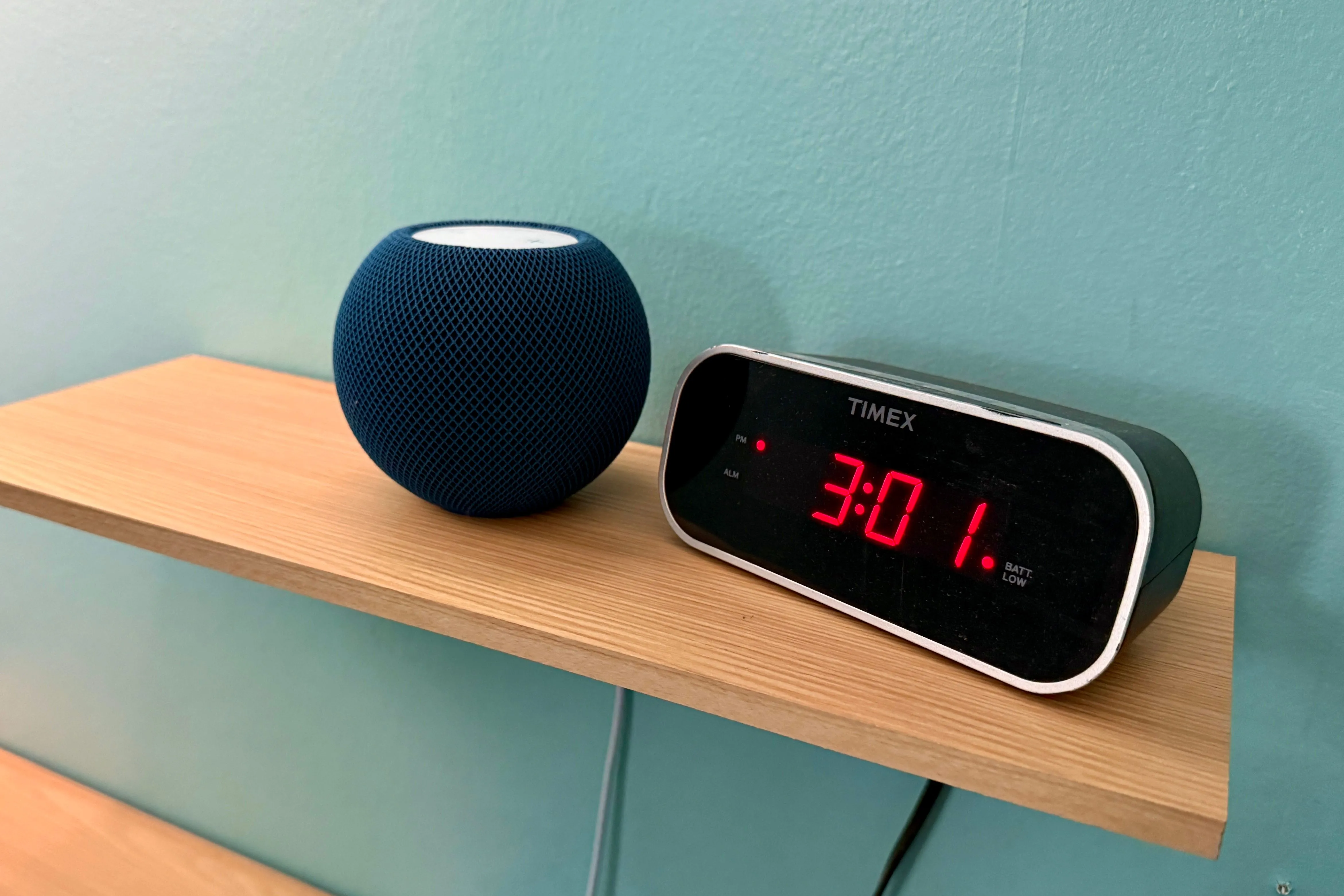 Loa thông minh Apple HomePod mini màu trắng đặt cạnh đồng hồ kỹ thuật số