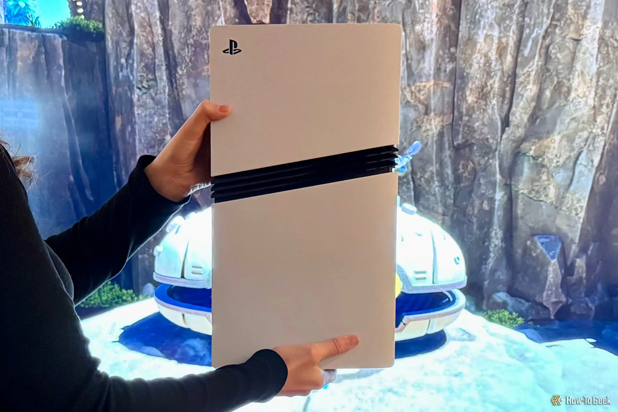 Một chiếc máy chơi game Sony PlayStation 5 Pro được cầm trên tay trước màn hình TV, so sánh khả năng đồ họa với PC gaming.