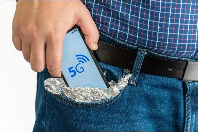 Người đàn ông bỏ smartphone bọc giấy bạc vào túi, minh họa quan ngại về sóng 5G.