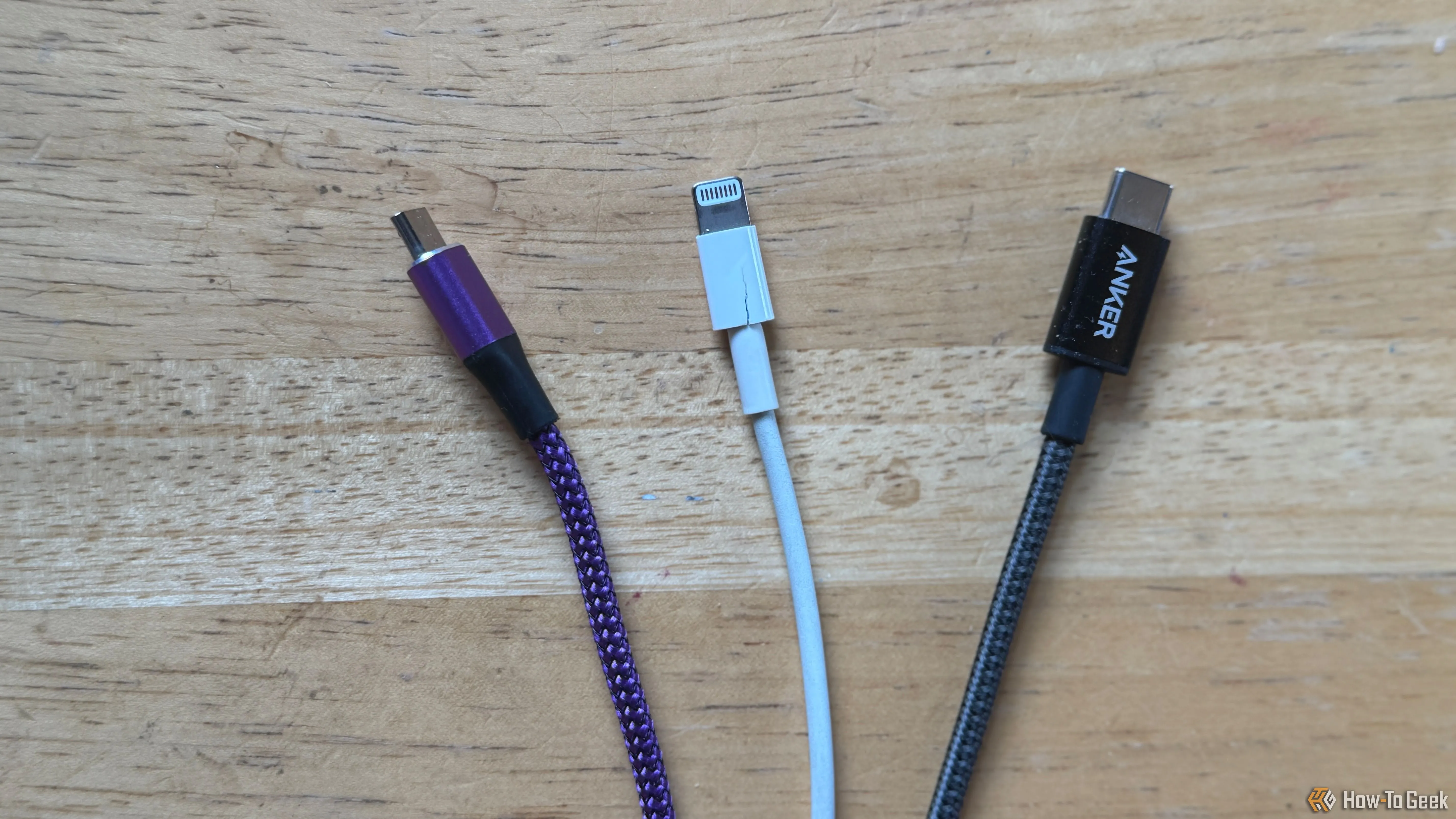 Ba loại cáp sạc khác nhau: cáp Micro-USB màu tím, cáp Lightning màu trắng và cáp USB-C màu xám được đặt trên bàn