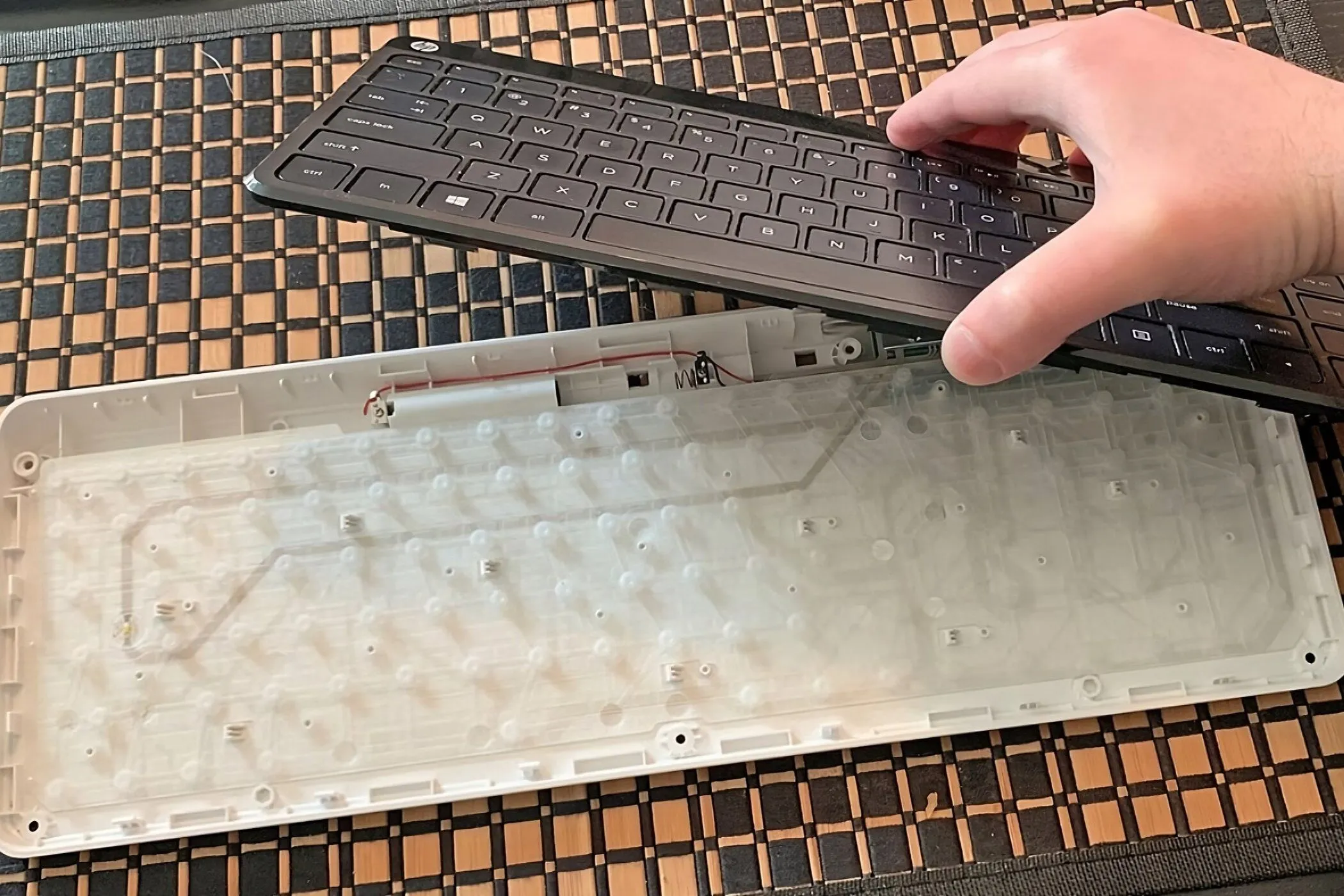 Bàn phím màng được tách làm hai phần với một bàn tay đang giữ các keycap phía trên màng