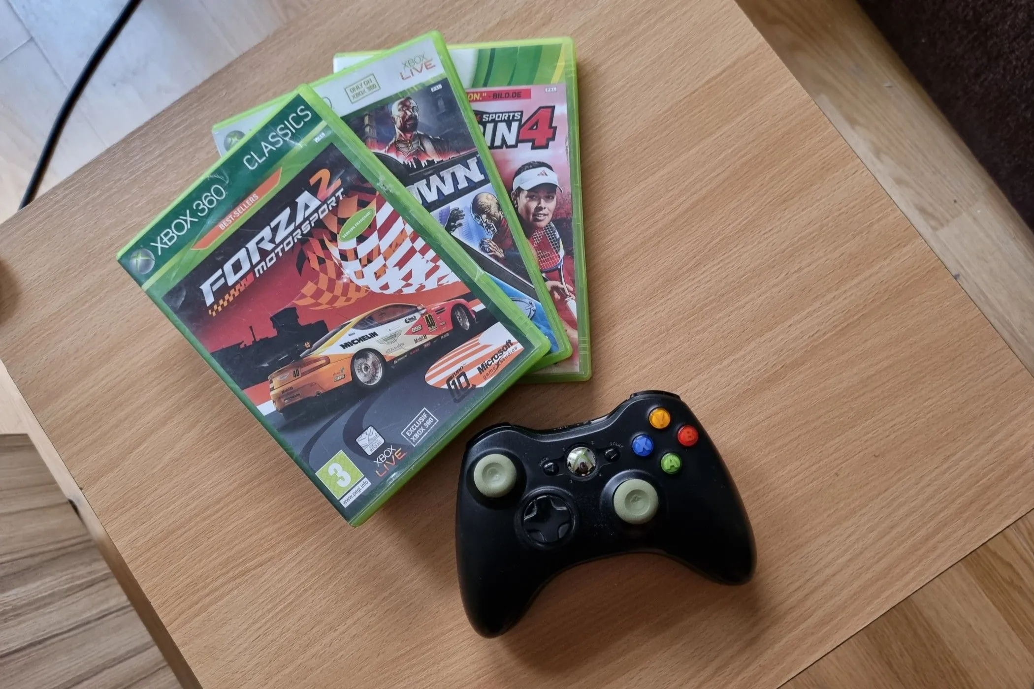 Các đĩa game Xbox 360 cùng một tay cầm Xbox 360 trên bàn.