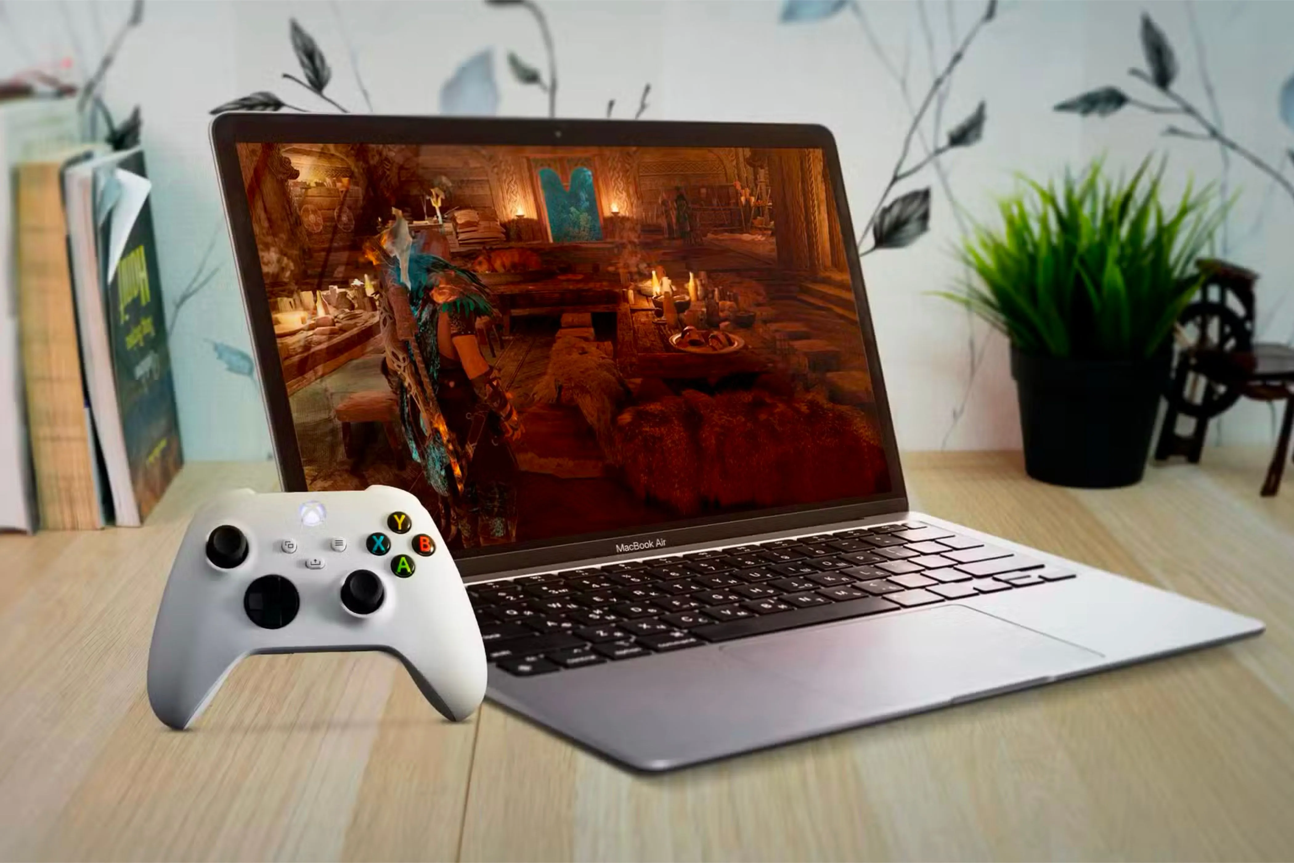 MacBook Air đặt dưới bàn gỗ, màn hình hiển thị game và tay cầm Xbox bên trái