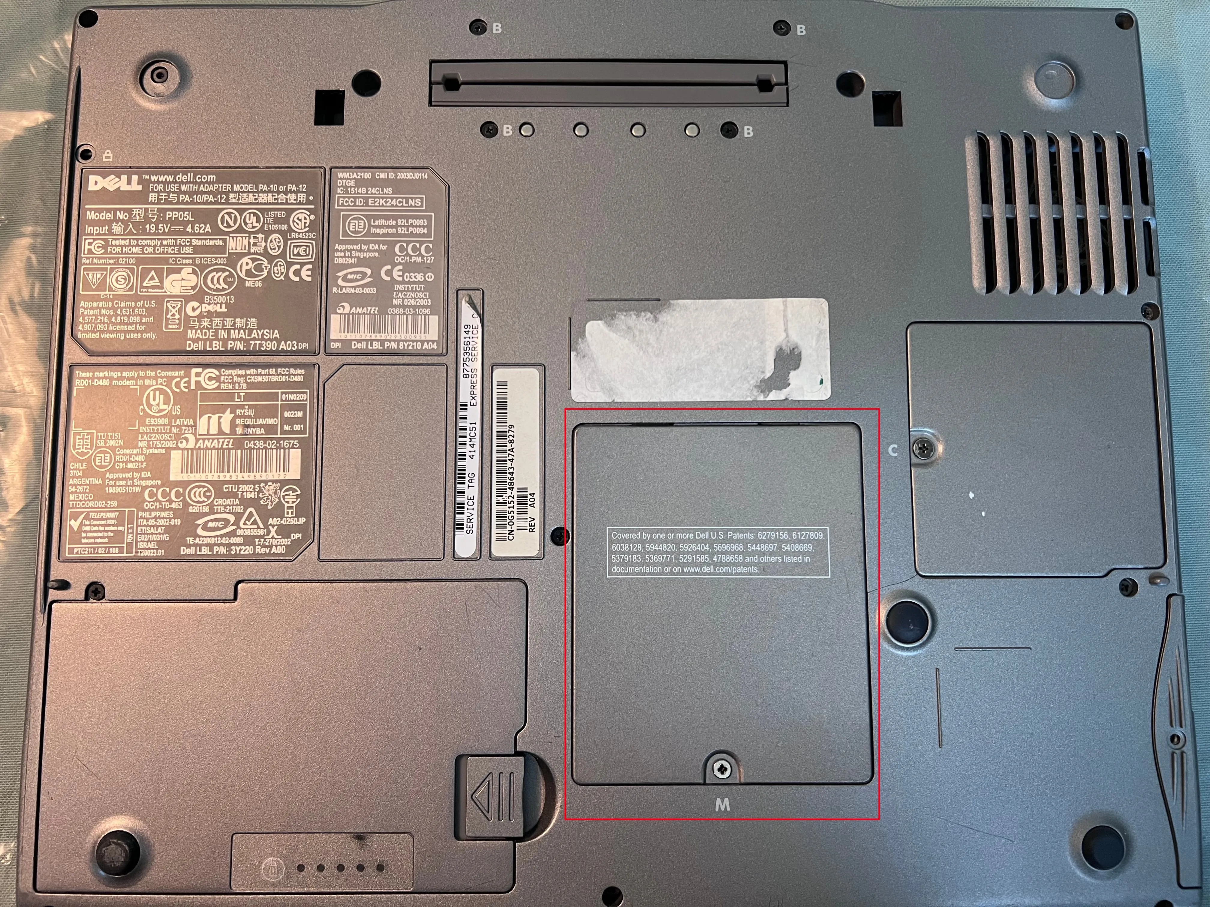 Mặt đáy laptop Dell với nắp che khe RAM được đánh dấu màu đỏ, chỉ vị trí cần tháo để nâng cấp RAM.