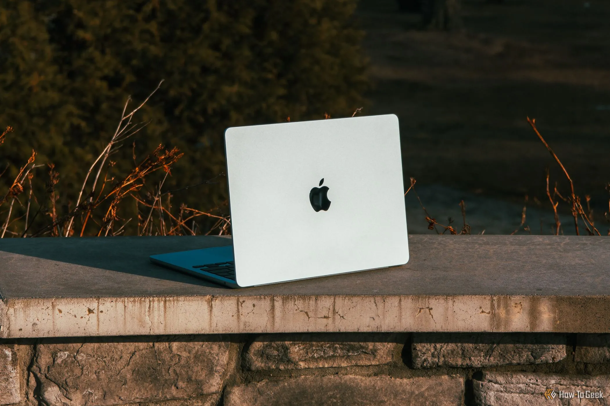 Mẫu MacBook Air M4 màu xanh da trời đặt nghiêng trên gờ bê tông dưới ánh nắng mặt trời.