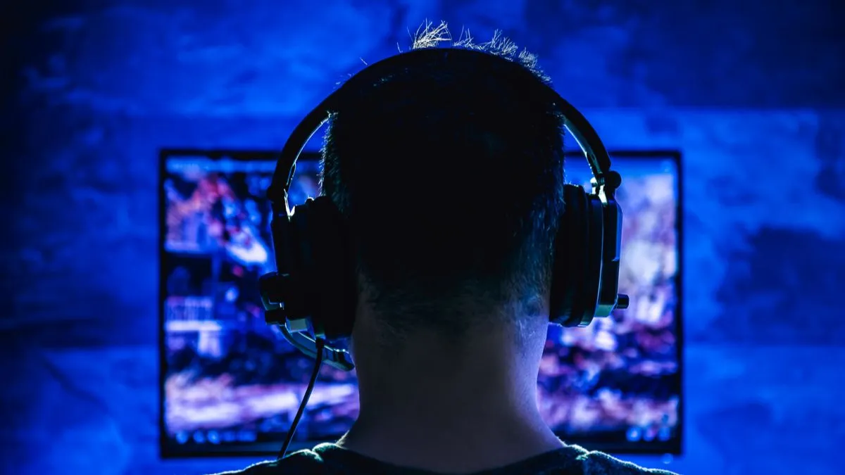 Một người đàn ông đeo tai nghe chơi game vào ban đêm trong căn phòng thiếu sáng, hình ảnh đối lập với thói quen chơi game buổi sáng có kiểm soát.
