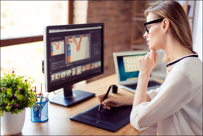 Một người phụ nữ đang nhìn màn hình máy tính và vẽ trên máy tính bảng kỹ thuật số