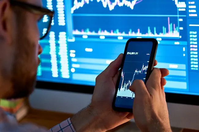 Người đàn ông giao dịch tài sản như cổ phiếu hoặc tiền điện tử trên điện thoại thông minh