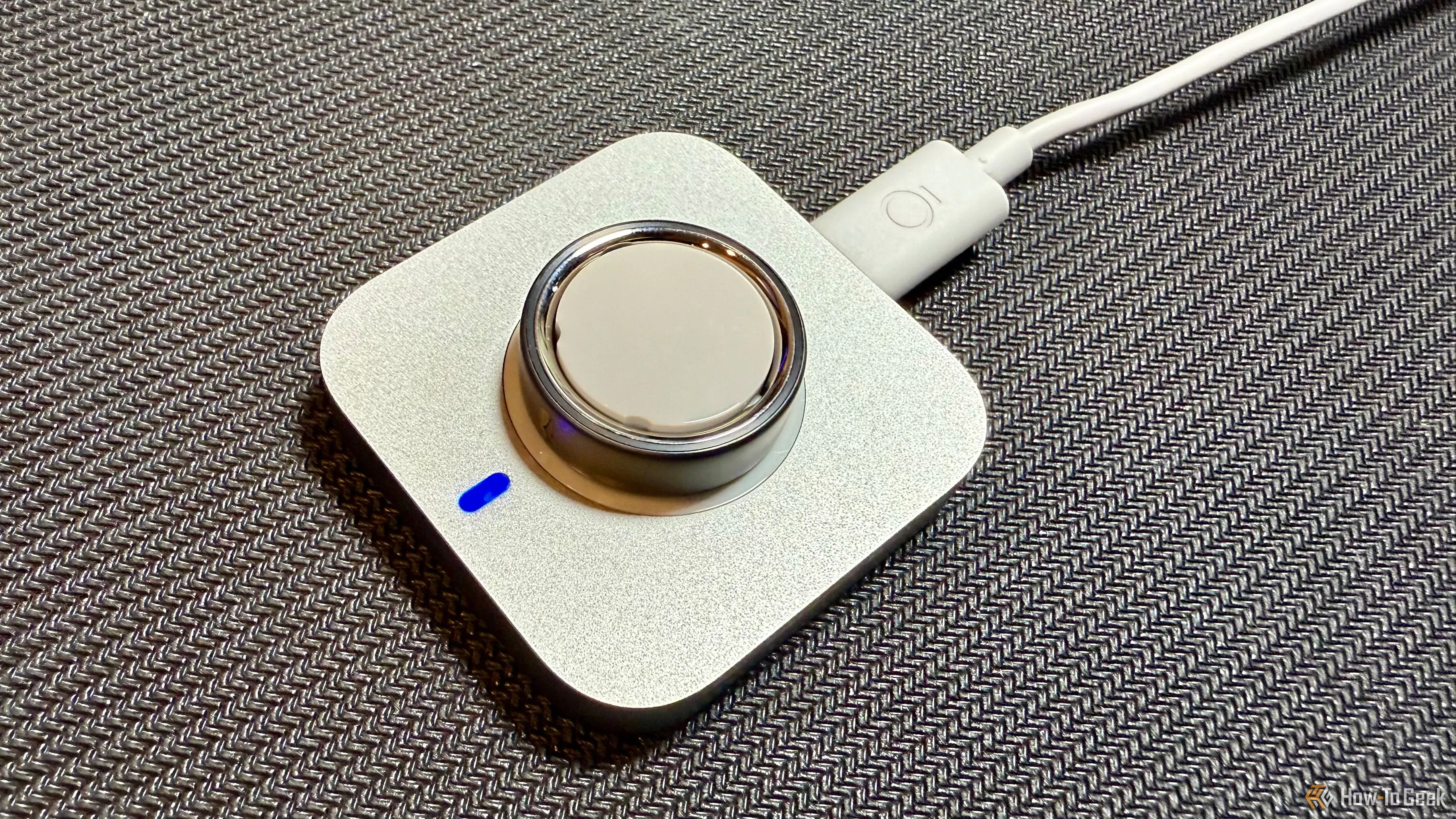 Nhẫn Oura Ring 4 đang được sạc trên đế sạc chuyên dụng, với đèn báo trạng thái màu xanh lá cây.