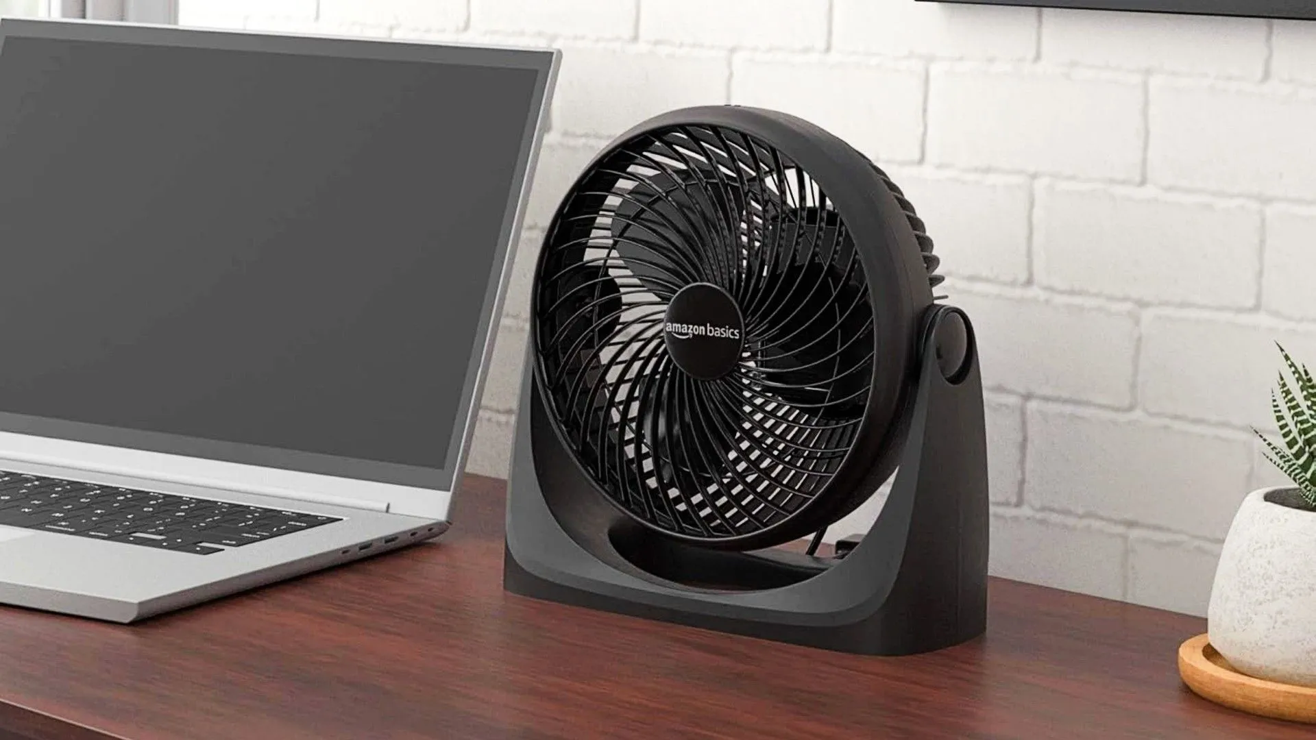 Quạt bàn Amazon Basics màu trắng được đặt trên bàn cạnh laptop, tạo luồng gió mát giúp làm việc thoải mái hơn.