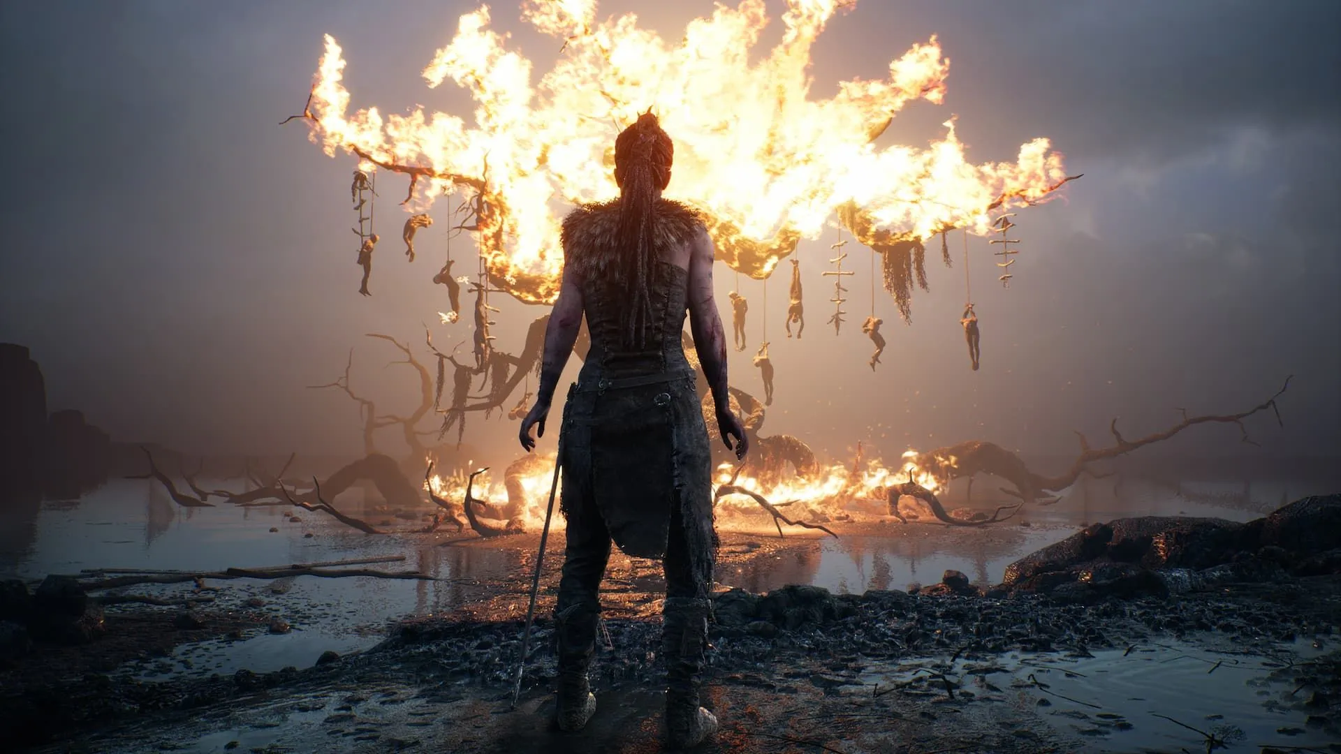 Senua đứng trước cây cháy rực trong Hellblade Senua’s Sacrifice, biểu tượng của sự hy sinh