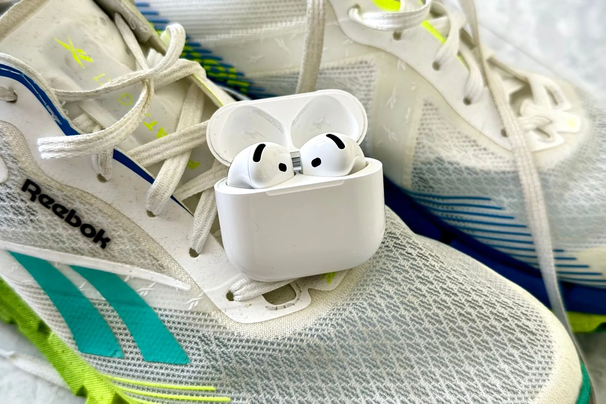 Tai nghe AirPods 4 màu trắng đặt cạnh đôi giày chạy bộ, gợi ý khả năng chống nước và độ bền khi tập luyện