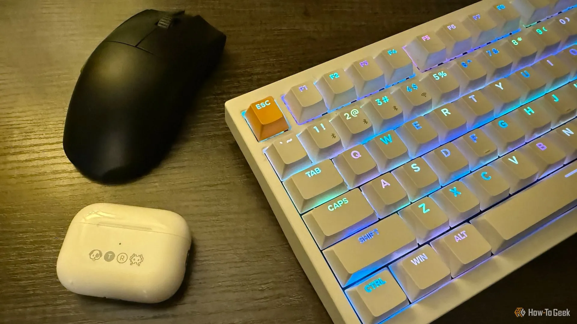 Tai nghe Apple AirPods Pro trong hộp đựng khắc họa, chuột không dây Razer Viper V3 Pro và bàn phím từ tính không dây Keychron K2 HE trên bàn, tạo nên một không gian làm việc công nghệ hiện đại.