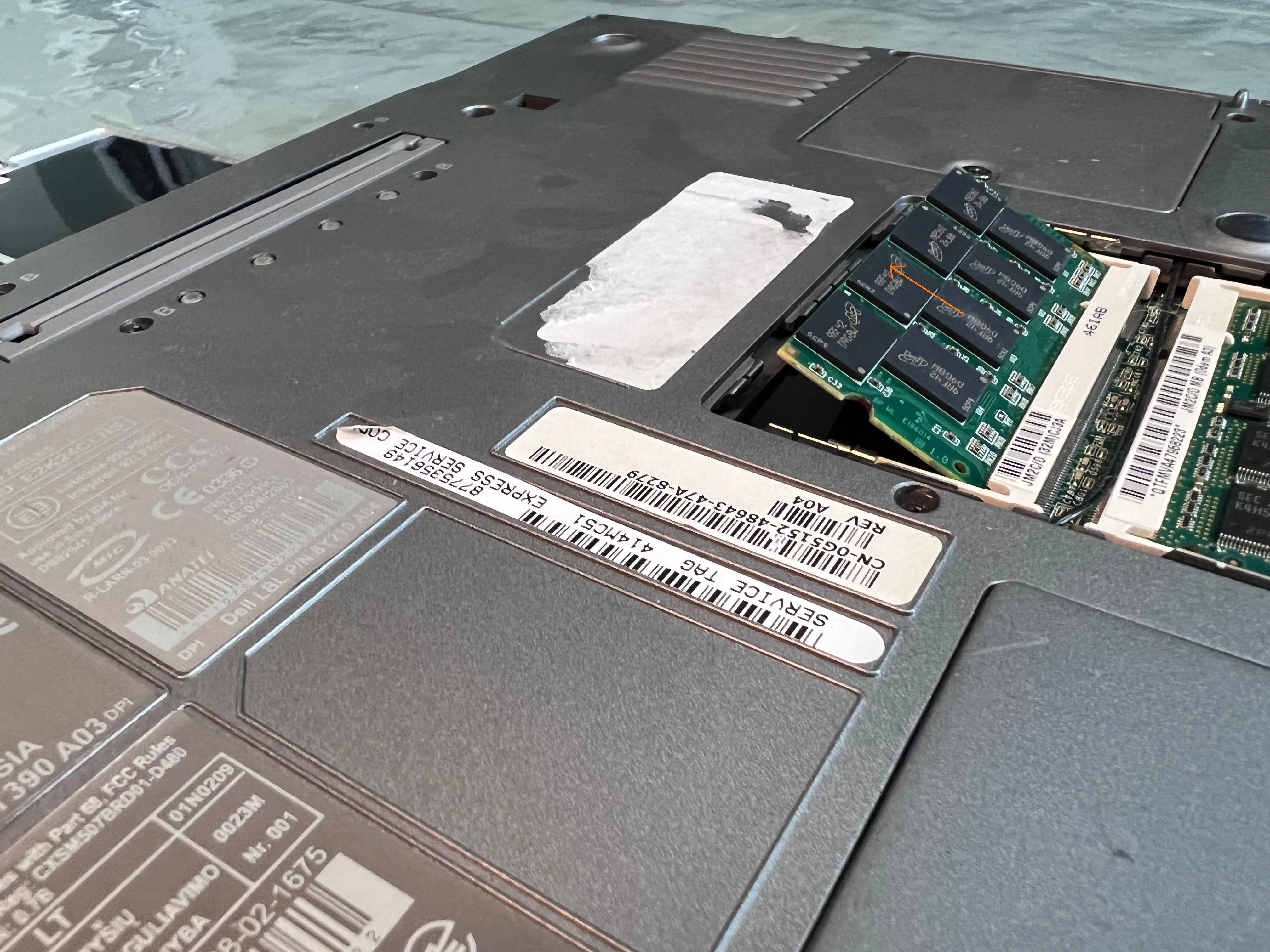 Thanh RAM trên laptop Dell đã được nhả chốt và nâng lên một góc, sẵn sàng để tháo ra khỏi khe cắm.