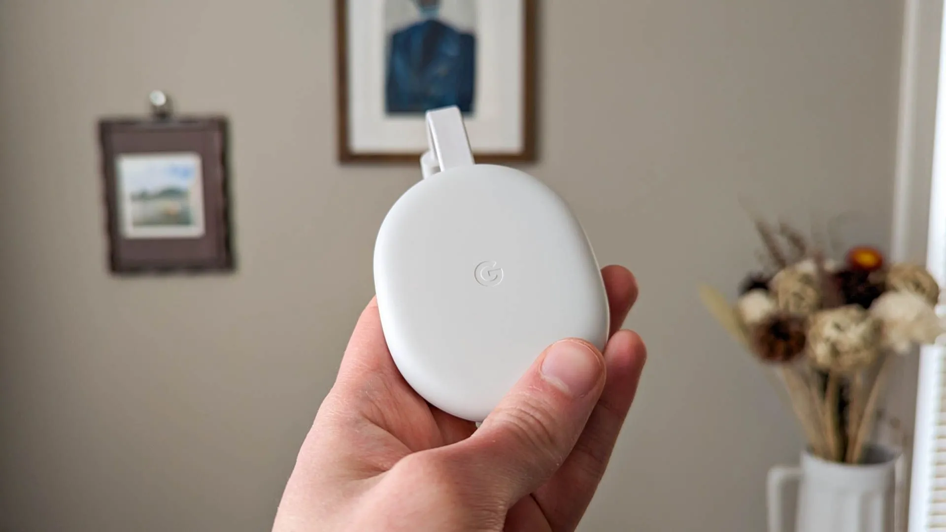 Thiết bị Google Chromecast màu trắng đặt trên bề mặt gỗ, gần một chiếc TV.