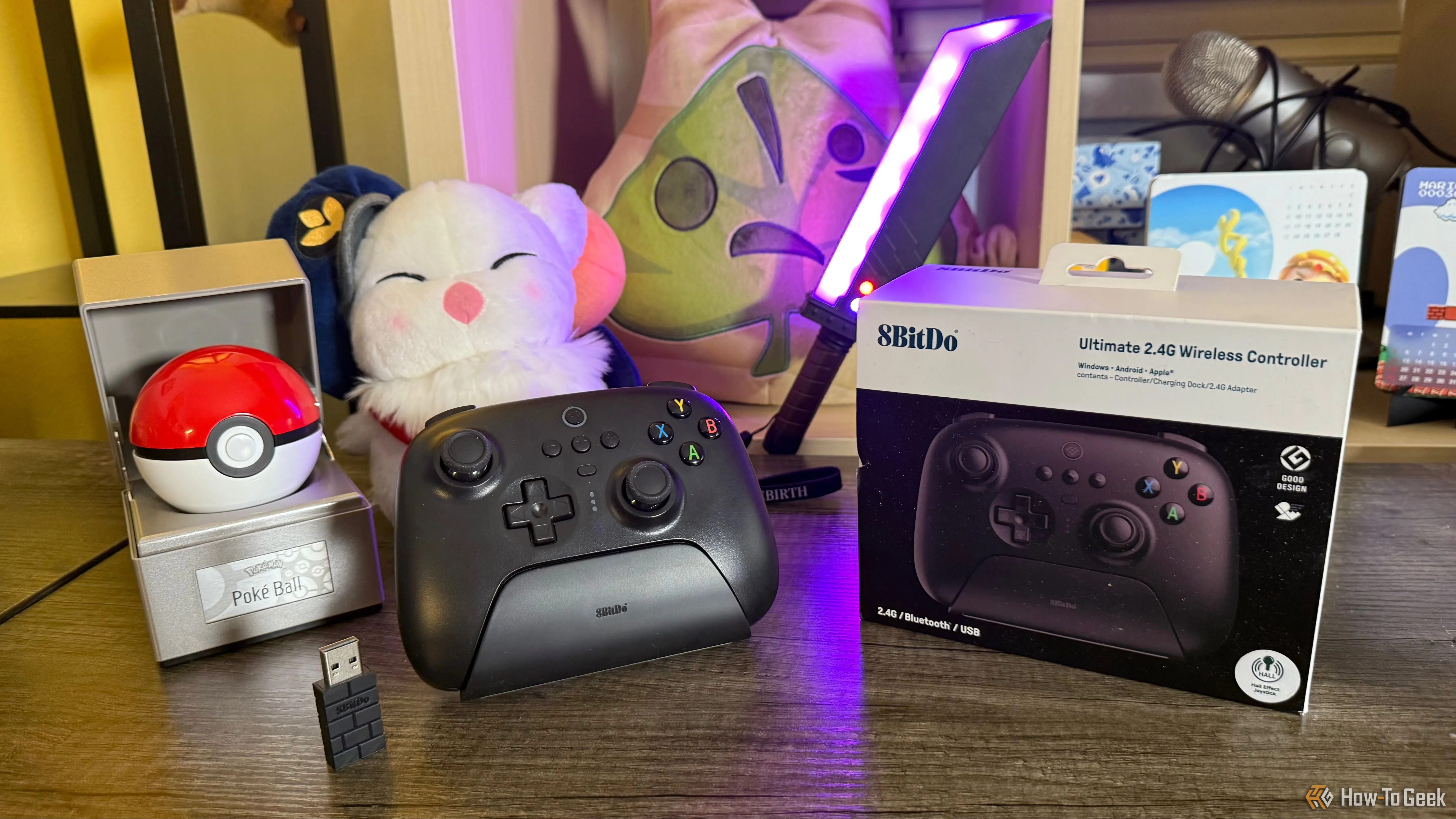 Toàn cảnh tay cầm 8BitDo Ultimate 2.4G cùng dock sạc, receiver và phụ kiện trên bàn, sẵn sàng cho trải nghiệm chơi game