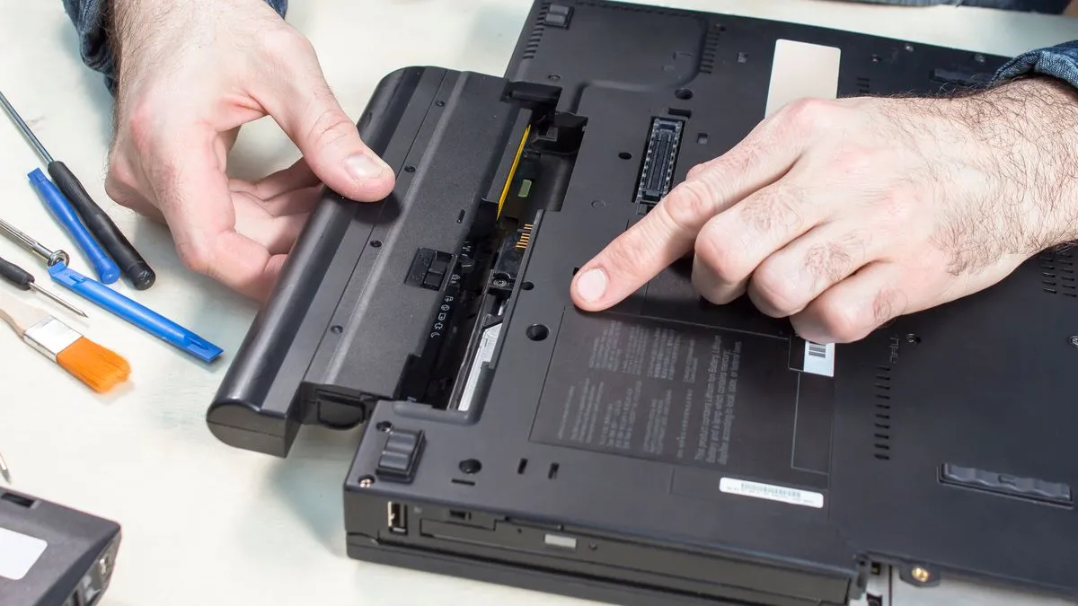 Một kỹ thuật viên đang kiểm tra và tháo pin ra khỏi một chiếc laptop, minh họa cho việc sửa chữa hoặc thay thế pin đúng cách.